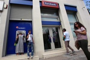 A woman makes a transaction at an ATM machine outside a Eurobank branch in central Athens